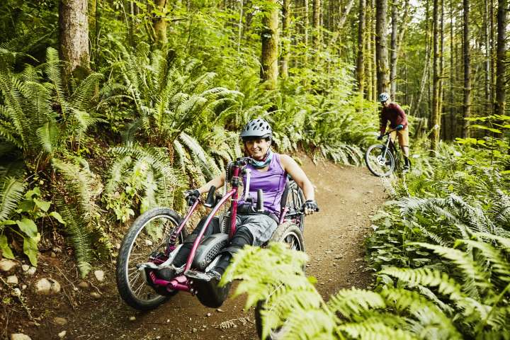Smiling female wheelchair athlete riding mountain bike on trail with friend